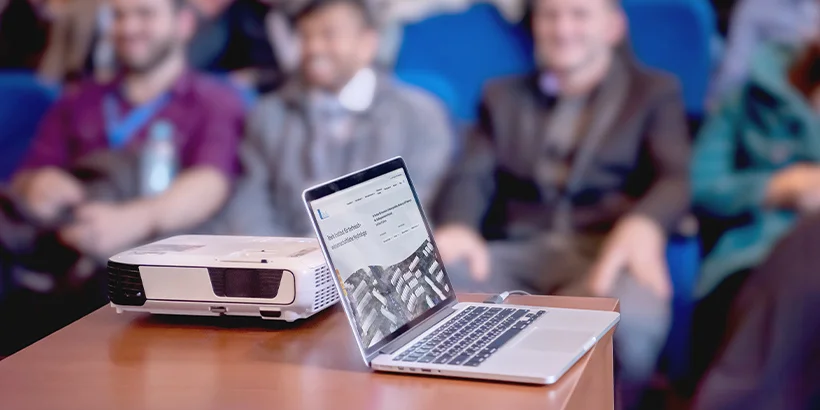Aufgeklappter Laptop vor Zuhörern eines Vortrags