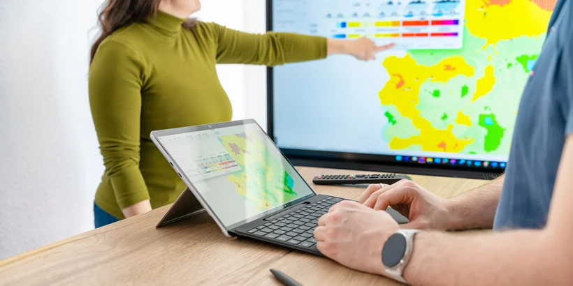 Eine Frau erklärt eine farbige Karte, während ein Mann am Laptop Eingaben macht.